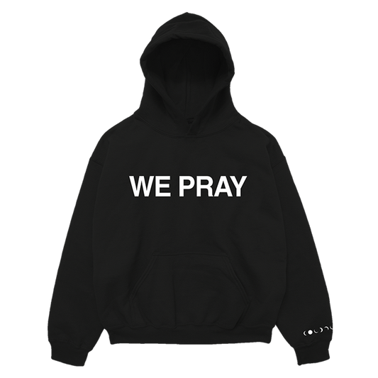 Front: WE PRAY is printed in large, white, bold letters across the chest of a black hoodie. Coldplay is spelled out in white phases of the moon on the wrist of the left sleeve. It also has a large center pocket at the waist.